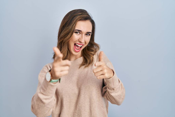 Young woman standing over isolated background pointing fingers to camera with happy and funny face. good energy and vibes.  - Foto, imagen