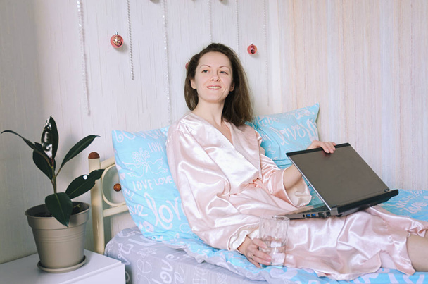 Young happy business woman lies in bed in pajamas in a cozy home. Online working, studying from home with laptop. Freelancer. Morning rituals.  - Photo, Image