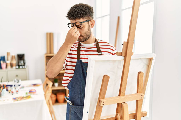 Jeune homme arabe au studio d'art fatigué se frottant le nez et les yeux ressentant fatigue et maux de tête. concept de stress et de frustration.  - Photo, image