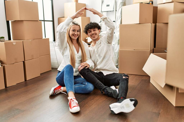 Jeune beau couple faisant symbole de la maison avec les bras levés à la nouvelle maison. - Photo, image