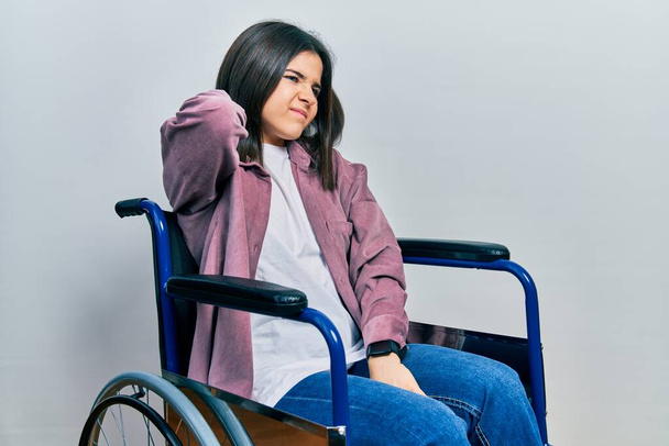 Mladá brunetka žena sedí na invalidním vozíku trpí bolestí krku, dotýká krku s rukou, svalové bolesti  - Fotografie, Obrázek