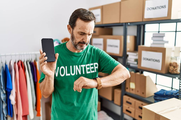 Mann mittleren Alters mit Bart und freiwilligem T-Shirt, Smartphone in der Hand und Armbanduhr, entspannt und selbstbewusst  - Foto, Bild