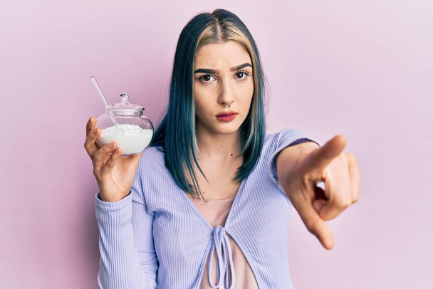 Mladá moderní dívka drží misku s cukrem ukazující prstem na fotoaparát a na vás, sebevědomé gesto vypadá vážně  - Fotografie, Obrázek