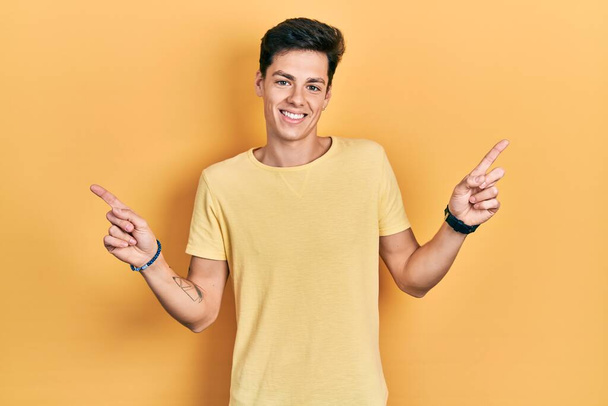 Giovane uomo ispanico indossa casual t shirt gialla sorridente fiducioso punta con le dita in direzioni diverse. copia spazio per la pubblicità  - Foto, immagini