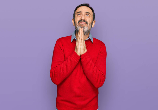 Hombre hispano de mediana edad vistiendo ropa casual mendigando y rezando con las manos juntas con expresión de esperanza en la cara muy emotiva y preocupada. mendicidad.  - Foto, Imagen