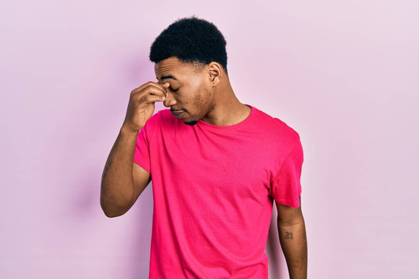 若いアフリカ系アメリカ人の男性は、疲れ摩擦鼻や目疲労や頭痛を感じカウアキャストシャツを着て。ストレスとフラストレーションの概念.  - 写真・画像