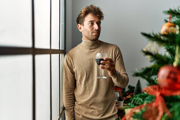若いですヒスパニック男飲むワインスタンディングによってクリスマスツリーにホーム - 写真・画像