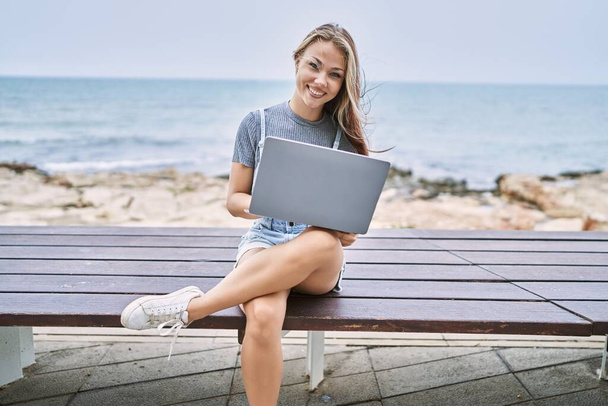 Young caucasian girl smiling happy using laptop sitting on the bench at the beach. - Fotografie, Obrázek