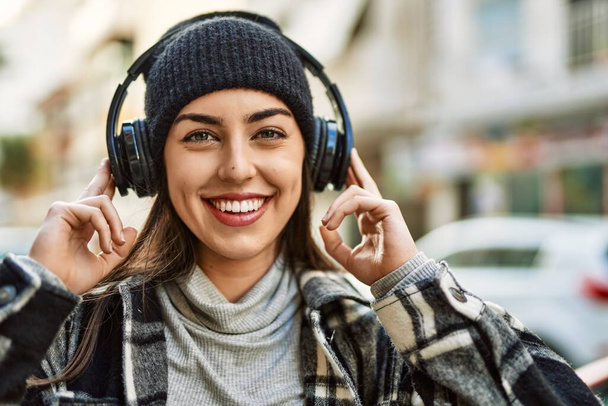 Jeune femme hispanique souriant heureux en utilisant des écouteurs à la ville. - Photo, image