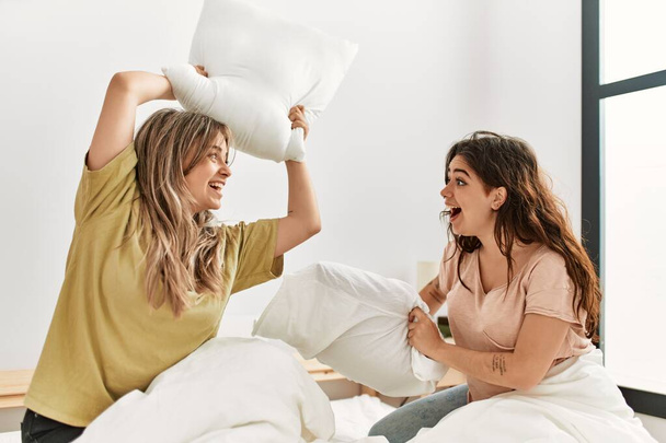 Mutlu gülümseyen genç çift evdeki yatakta yastıklarla kavga ediyor.. - Fotoğraf, Görsel