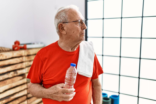 Старший мужчина в спортивной одежде и полотенце в тренажерном зале глядя в сторону, расслабиться профиль позировать с естественным лицом и уверенной улыбкой.  - Фото, изображение