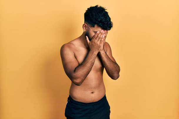 Arab man with beard wearing swimwear shirtless with sad expression covering face with hands while crying. depression concept.  - Photo, image