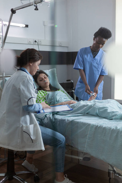 病院のベッドで患者に診断を説明するクリップボード上の研究室の結果を指す医療 - 写真・画像