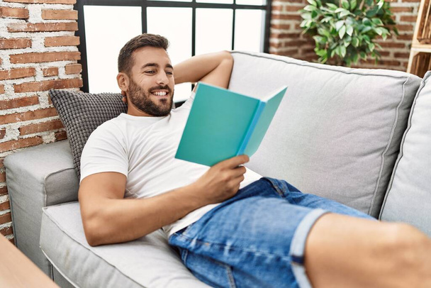 Jeune homme hispanique souriant livre de lecture confiant à la maison - Photo, image