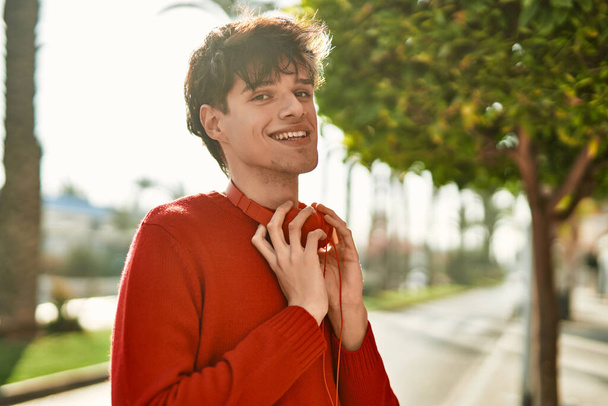 Молодий іспаномовний чоловік посміхається щасливим, використовуючи навушники в місті
 - Фото, зображення