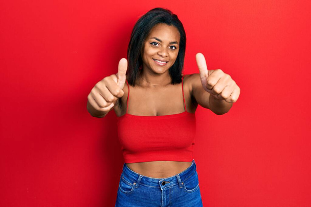 Молода афроамериканська дівчина, одягнена в повсякденний стиль з безрукавною сорочкою, схвалюючи позитивний жест рукою, великі пальці посміхаються і щасливі за успіх. жест переможця.  - Фото, зображення