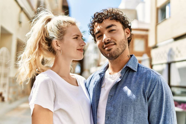 Mladá krásná dvojice kavkazské přítelkyně a hispánský přítel objímající se v lásce venku za slunečného dne. Žena a muž se usmívá šťastný vztah - Fotografie, Obrázek