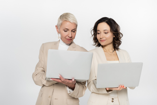 Senior businesswoman holding laptop near colleague isolated on grey  - Foto, afbeelding