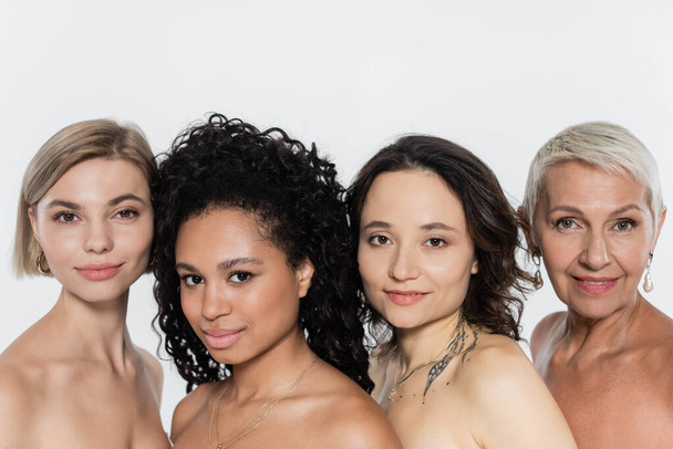 Positive interracial women with naked shoulders looking at camera isolated on grey  - 写真・画像
