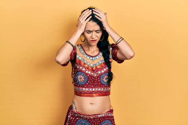 Young woman wearing bindi and bollywood clothing suffering from headache desperate and stressed because pain and migraine. hands on head.  - Foto, imagen