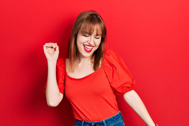 Zrzka mladá žena na sobě ležérní červené tričko tanec šťastný a veselý, úsměv pohybující ležérní a sebevědomý poslech hudby  - Fotografie, Obrázek