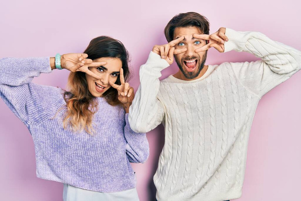 Jeune couple hispanique portant des vêtements décontractés faisant symbole de paix avec les doigts sur le visage, souriant joyeux montrant la victoire  - Photo, image