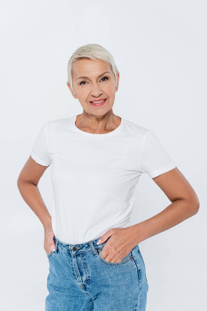 Positive senior woman in t-shirt and jeans posing isolated on grey  - Foto, Bild
