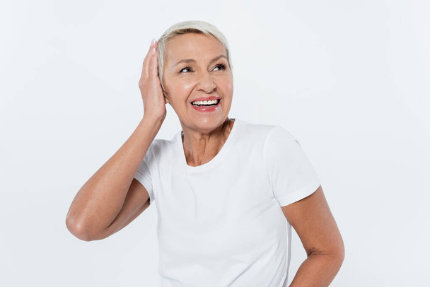 Feliz mujer mayor tocando la cabeza aislada en gris  - Foto, Imagen