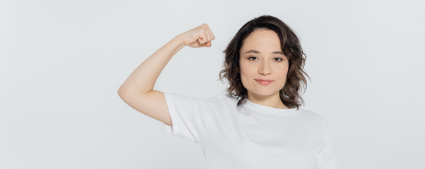 Brunette woman showing muscles and looking at camera isolated on grey, banner  - Photo, image