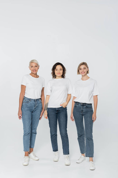 Full length of smiling women in white t-shirts standing on grey background  - Foto, Bild