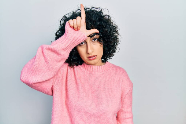 Mladá žena z Blízkého východu nosí ležérní oblečení a dělá si legraci z lidí s prsty na čele, kteří dělají posměšné a urážlivé gesto.  - Fotografie, Obrázek