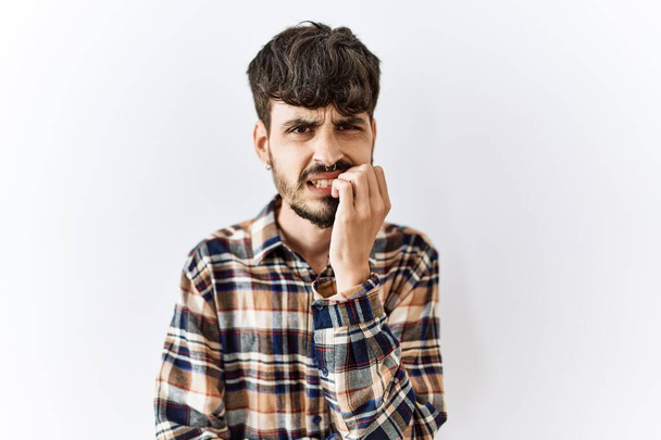Spanyol férfi szakállal, elszigetelt háttér fölött áll, stresszesnek és idegesnek tűnik, miközben a kezei körmöket harapdálnak. szorongás.  - Fotó, kép