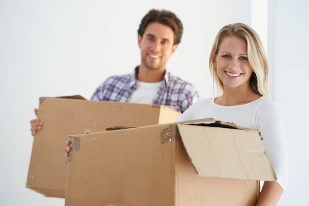 Listo para hacer nuevos recuerdos en su primer hogar. Retrato de una feliz pareja llevando cajas de cartón marrón en su nuevo hogar. - Foto, Imagen
