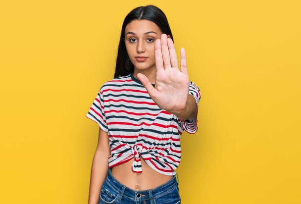 Young hispanic girl wearing casual clothes doing stop sing with palm of the hand. warning expression with negative and serious gesture on the face.  - Photo, Image
