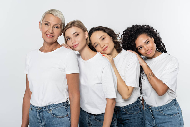 Young multiethnic women in white t-shirts hugging near smiling friend isolated on grey, feminism concept - Φωτογραφία, εικόνα
