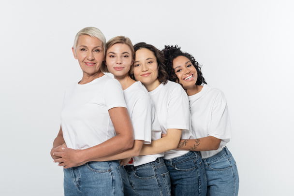 Cheerful interracial women in white t-shirts hugging each other isolated on grey  - Foto, afbeelding