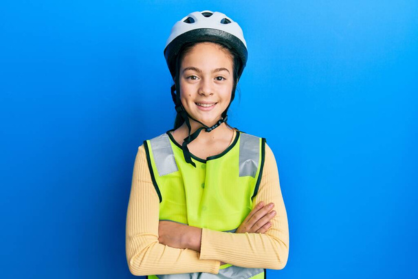 Piękna brunetka dziewczynka w kasku rowerowym i odblaskowej kamizelce szczęśliwa twarz uśmiechnięta skrzyżowanymi ramionami patrzącymi w kamerę. osoba pozytywna.  - Zdjęcie, obraz