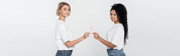 Mujeres multiétnicas con camisetas blancas con cinta de sensibilización sobre el cáncer de mama aisladas en una pancarta gris   - Foto, imagen