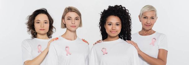Multiethnic women with pink ribbons looking at camera isolated on grey, banner  - Photo, image