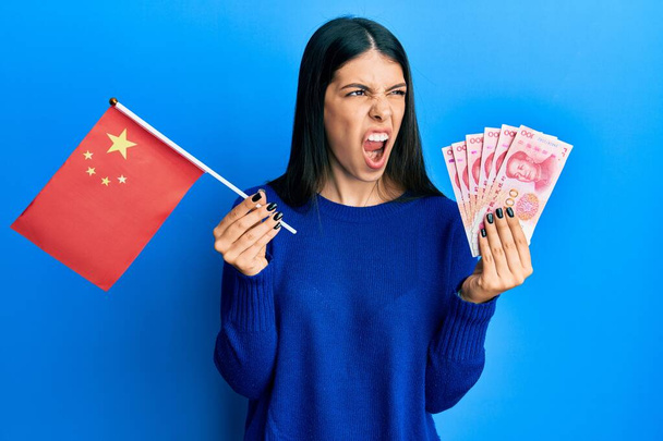 Fiatal spanyol nő kezében porcelán zászló és jüan bankjegyek dühös és őrült sikoltozó frusztrált és dühös, kiabált a harag. düh és agresszív koncepció.  - Fotó, kép