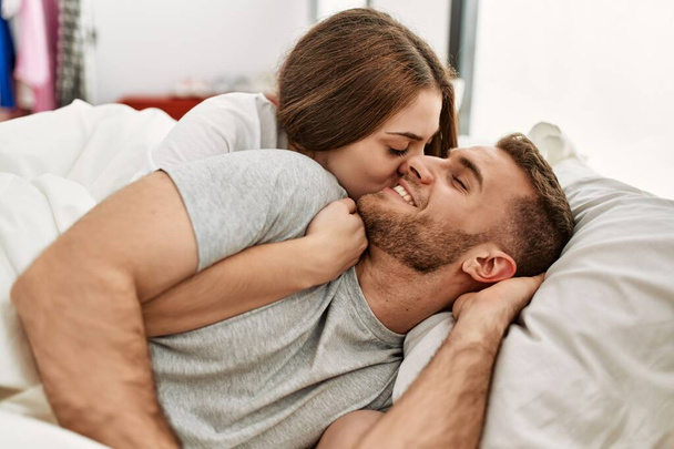Молодая кавказская пара улыбается счастливые объятия на кровати дома. - Фото, изображение