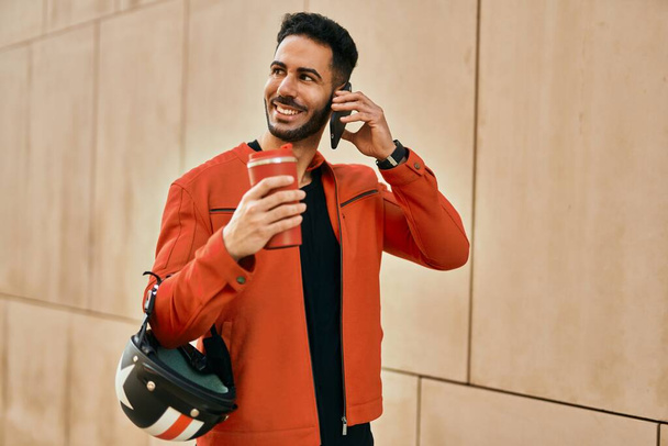 Giovane uomo ispanico che parla sullo smartphone bevendo caffè in città. - Foto, immagini