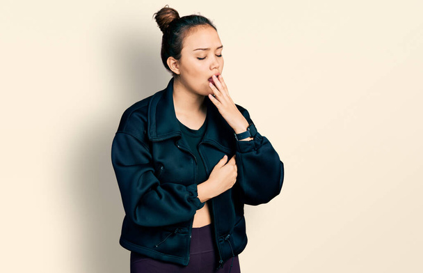 Joven chica hispana usando ropa deportiva aburrida bostezando cansada cubriendo la boca con la mano. inquietud y somnolencia.  - Foto, imagen