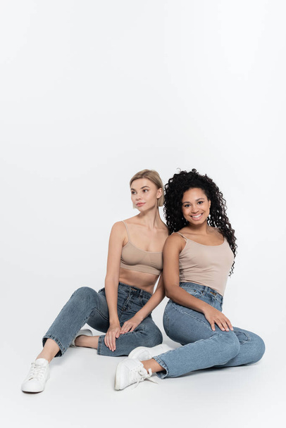Smiling african american woman sitting near friend on grey background, feminism concept - Photo, Image