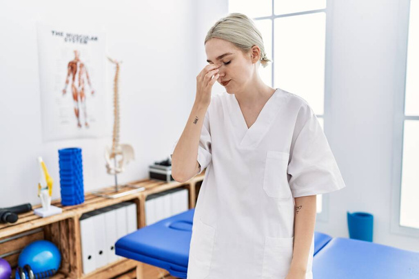 Young caucasian woman working at pain recovery clinic tired rubbing nose and eyes feeling fatigue and headache. stress and frustration concept.  - Foto, Imagem
