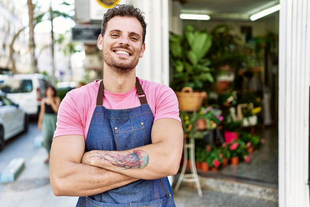 Young hispanic worker wearing apron standing with arms crossed gesture at the florist. - Photo, Image
