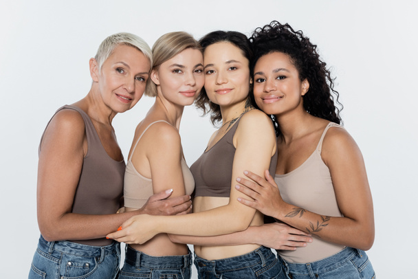 Mulheres multiétnicas abraçando e sorrindo para a câmera isolada no conceito cinza, feminismo - Foto, Imagem
