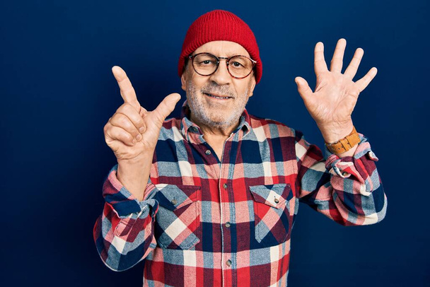 bel homme mature portant look hipster avec bonnet en laine montrant et pointant vers le haut avec les doigts numéro sept tout en souriant confiant et heureux.  - Photo, image