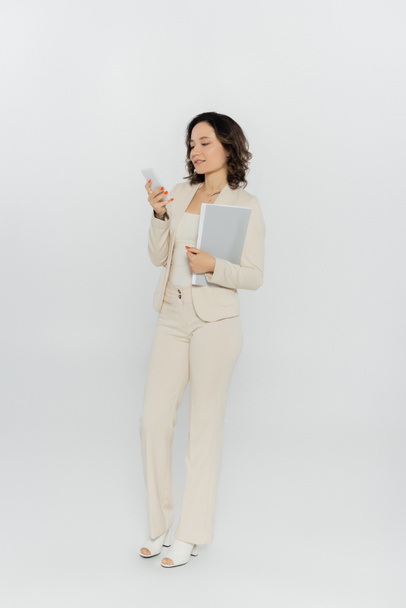 Businesswoman holding paper folder and using smartphone on grey background  - Fotoğraf, Görsel