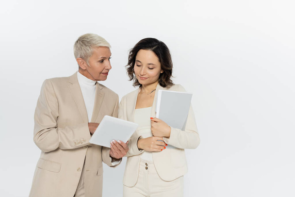 Senior businesswoman holding digital tablet near colleague with paper folder isolated on grey  - Foto, immagini